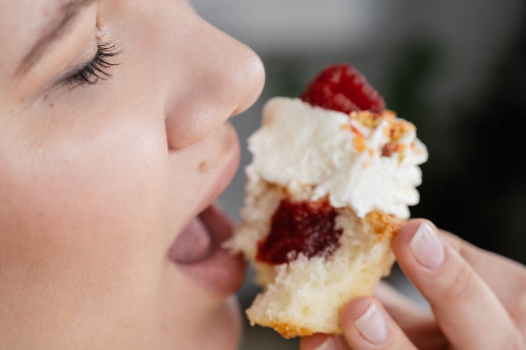 woman biting delicious cupcake with berries and cream